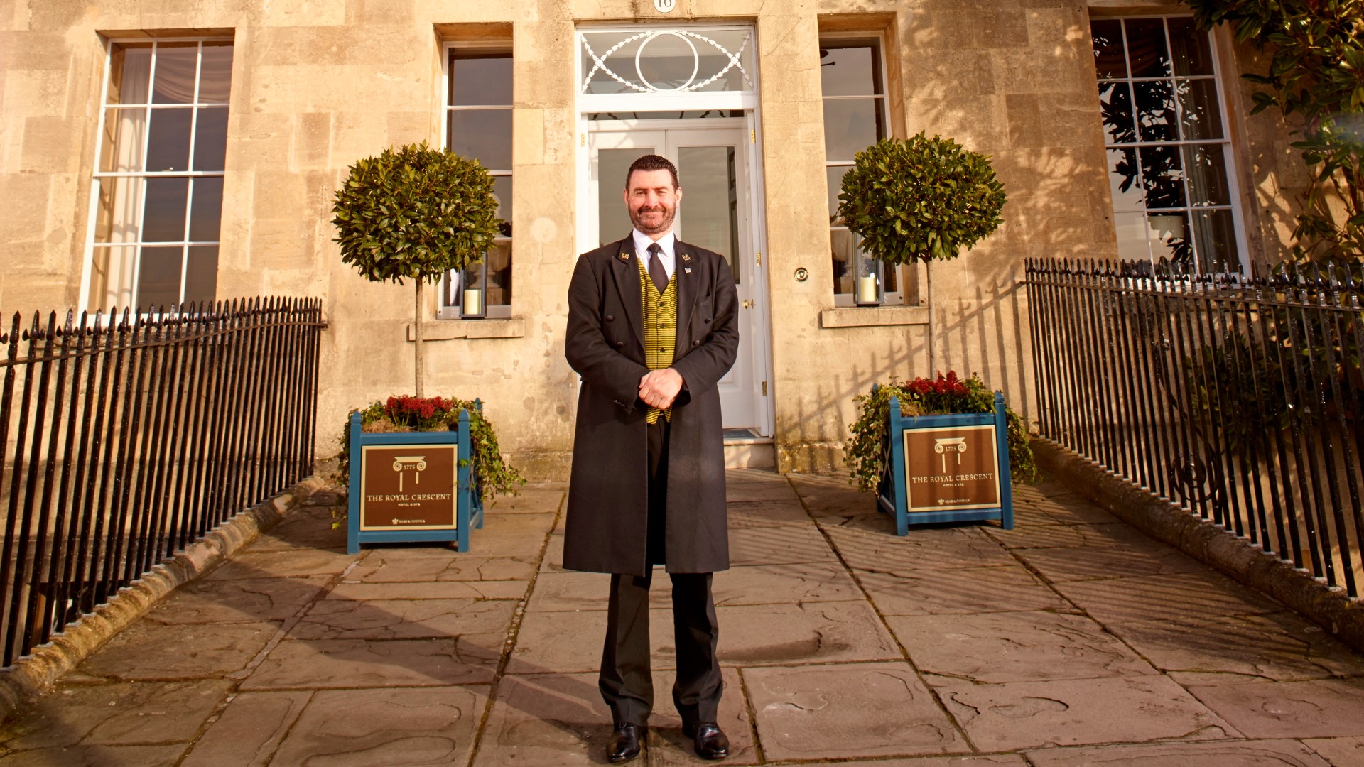 Smiling doorman stands outside of The Royal Crescent Hotel & Spa